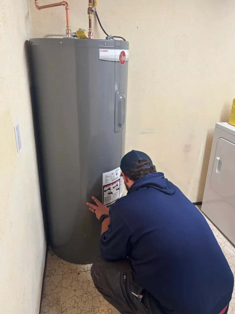 Technician crouching in front of a Rheem water heater and inspecting a label